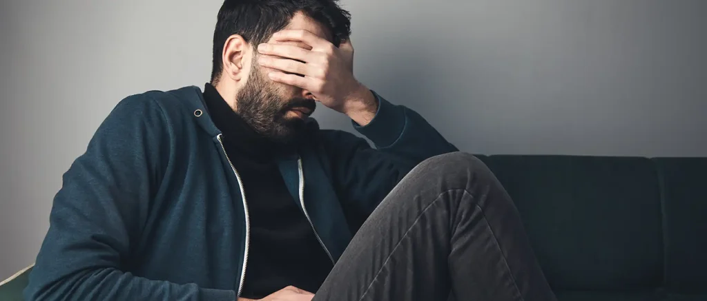 Sad man covered his face sitting sofa.