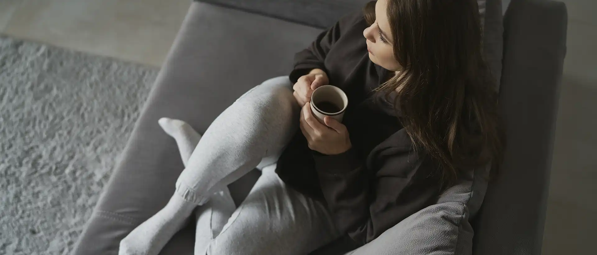 Woman sits on sofa drinking coffee 