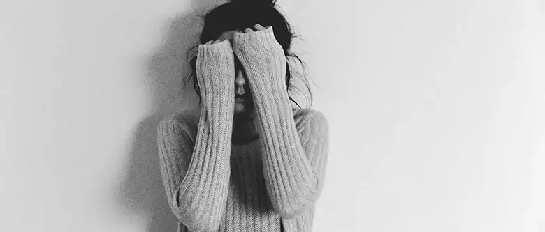 Teenage girl hiding face while standing against white background.